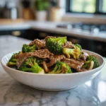 Beef and broccoli stir-fry in a white bowl with sesame sauce and vibrant vegetables